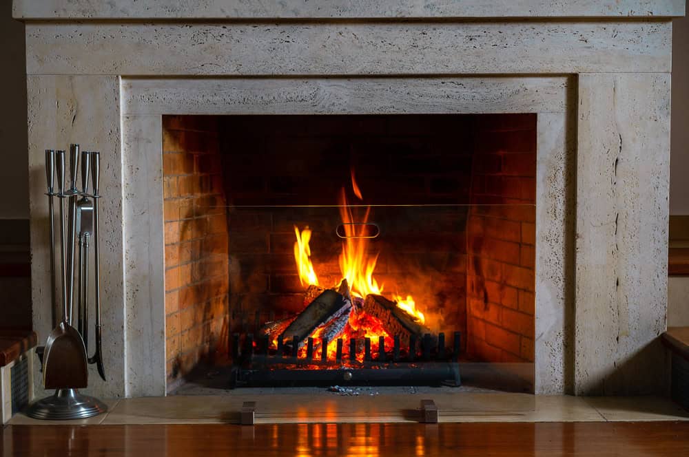A stone fireplace with a burning fire, logs stacked on a metal grate, and fireplace tools standing to the side. Warm orange flames and glowing embers create a cozy atmosphere—perfect inspiration for Chimney Repair Providence County, RI.