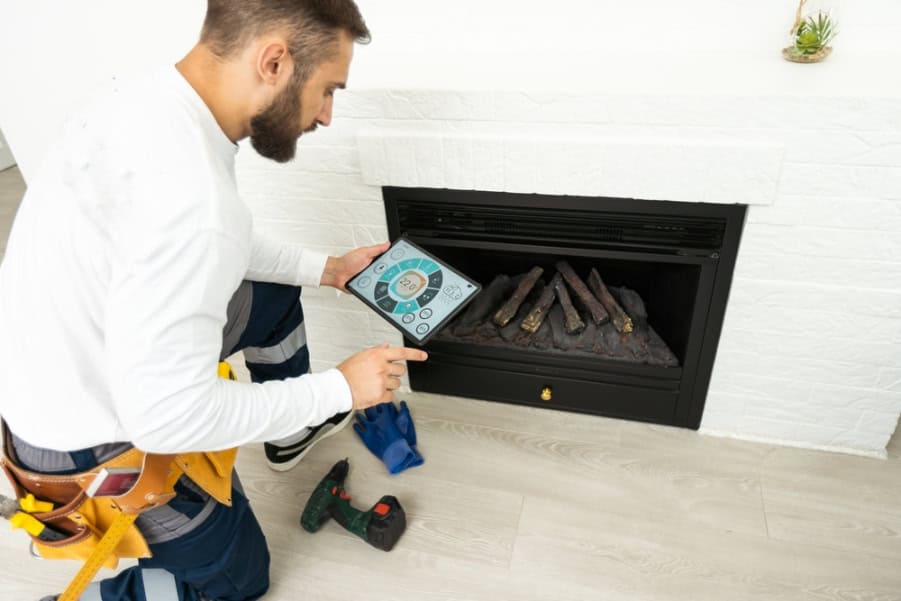 A technician kneels by a gas fireplace, using a tablet for diagnostics. Tools, including a cordless drill and gloves, are nearby. The bright room hints at expert Chimney Repair in Providence County, RI for safe and reliable service.