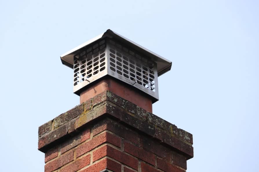 A close-up view of a brick chimney with a metal cap and mesh screen on top, set against a clear blue sky—perfect for highlighting Chimney Cleaning Providence County, RI services.